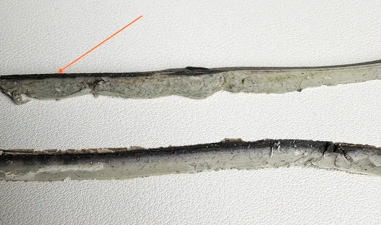 Hand mit schwarzem Handschuh reinigt Silikonfugen zwischen weißen Fliesen mit einem gelben Reinigungsschwamm
